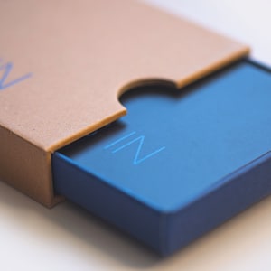 May include: A blue box with the word "IN" printed on the top. The box is partially open, revealing a brown cardboard box underneath.