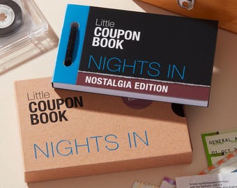 May include: A Little Coupon Book Nights In Nostalgia Edition with a black, blue, and maroon cover, featuring a black spiral binding. Below it sits a matching tan cardboard box labeled Little Coupon Book Nights In in blue and black text.