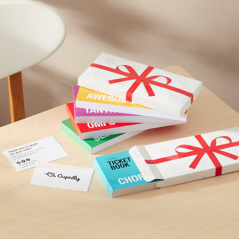 May include: A stack of colorful gift boxes with red ribbon bows. The top box is white with a red ribbon bow and the text "Little Ticket Book" on the front. The box is open and the inside is blue with the text "CHOP" on the front.