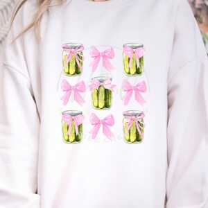 May include: White sweatshirt featuring a design of pickle jars tied with pink bows.
