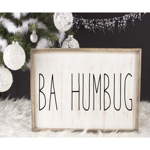 May include: A white wooden sign with a black frame and the text "BA HUMBUG" written in a simple, modern font.