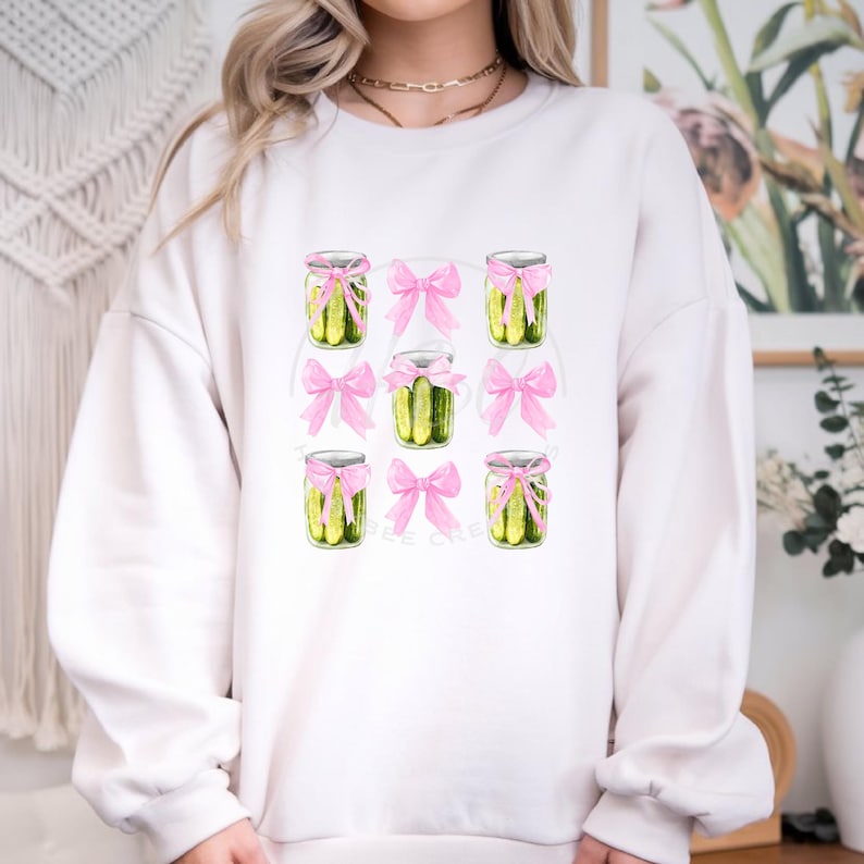 May include: White sweatshirt featuring a design of pickle jars tied with pink bows.