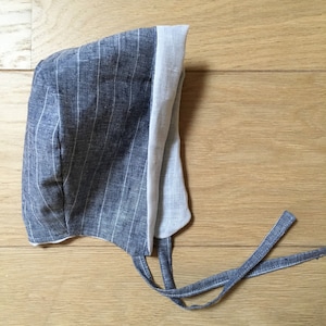 May include: A blue and white striped bonnet with a white lining and ties. The bonnet is made of a soft, lightweight fabric.