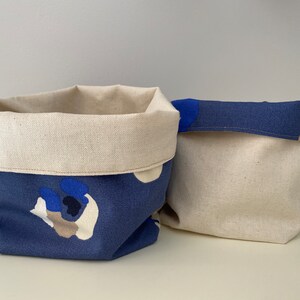 Puede incluir: Dos cestas de almacenamiento de tela con un patrón abstracto azul y blanco. Las cestas están hechas de una tela suave y natural y tienen un forro de color crema.