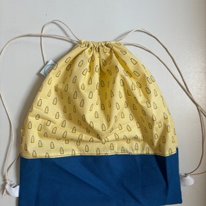 Könnte beinhalten: Eine gelbe Kordeltasche mit blauem Boden. Die Tasche hat ein Muster aus kleinen gelben Flaschen auf dem gelben Teil.