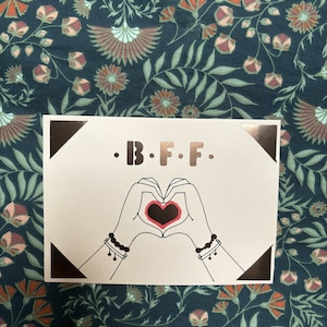 Carte de vœux élégante “B.F.F.” avec un design artistique représentant deux mains formant un cœur. Idéale pour célébrer l’amitié.