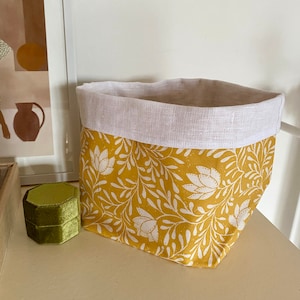 Peut inclure: Un panier de rangement en tissu jaune avec un motif floral blanc. Le panier est doublé de lin blanc.