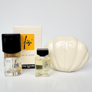 Puede incluir: Dos pequeños frascos de perfume Guy Laroche Fidji con tapas negras, una caja con el logo Fidji y una pieza decorativa de cerámica blanca. Los frascos de perfume están etiquetados como "ATOMISEUR PARFUM" y "EAU DE TOILETTE".