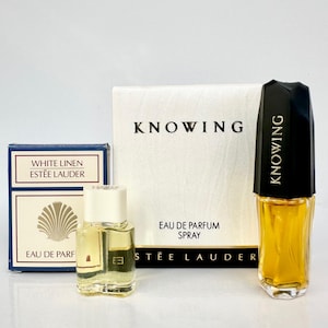 May include: A selection of Estée Lauder perfumes, featuring a small bottle of White Linen and two bottles of Knowing. The Knowing bottles have black caps and the boxes display the name. The perfumes are presented on a white surface.