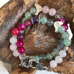 Peut inclure: Bracelet de perles avec des pierres précieuses colorées, notamment des perles roses, vertes et violettes. Le bracelet est orné d'éléments argentés et d'un fermoir décoratif. Deux breloques argentées en forme de phoque.