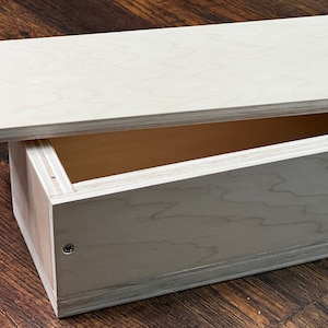 May include: A wooden box with a hinged lid, made of light-colored wood with a natural grain pattern. The lid is open, revealing the empty interior of the box.