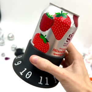 May include: A black can holder with a silver can of unsweetened mixed berry sparkling water. The can has a red strawberry and a red raspberry on it. The can holder has numbers 8, 9, 10, and 11 printed on it.