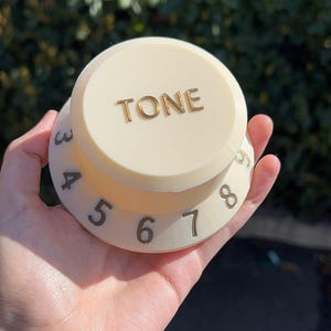 May include: A white plastic knob with the word "TONE" printed in gold lettering. The knob has numbers 3 through 8 printed around the edge in gold.