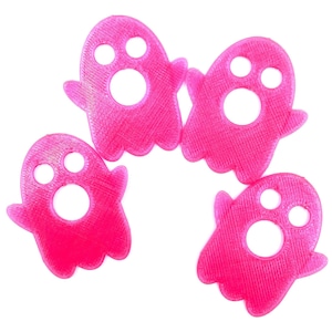 May include: Four pink plastic ghost-shaped ornaments with a textured surface. Each ghost has a large circle and two smaller circles cut out to resemble a face.