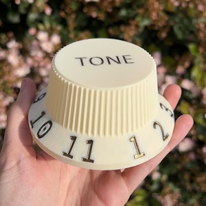 May include: A white plastic knob with the word "TONE" printed on the top and numbers 10, 11, 1, 2, and 3 printed around the base.