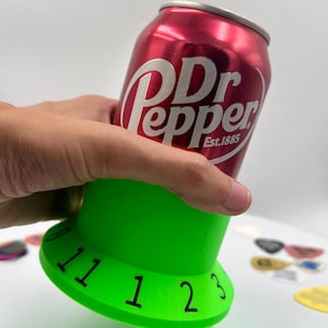May include: A green plastic can holder with numbers 11, 1, 2, and 3 printed on the side. A red can of Dr Pepper is sitting on top of the holder.