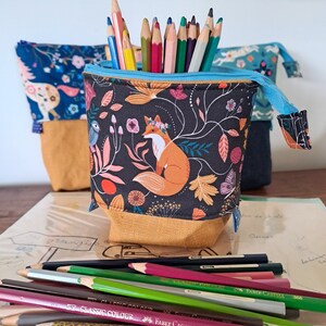 Peut inclure: Une trousse à crayons colorée avec un imprimé de renard et de fleurs. La trousse est en tissu et possède une fermeture à glissière. Elle est remplie de crayons de couleur.