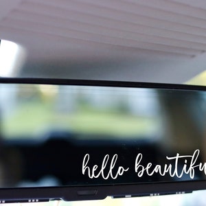 May include: A rearview mirror with the text "hello beautiful" written in white cursive lettering on the glass.