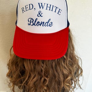May include: A trucker hat with a white front panel, a red brim, and a navy blue mesh back. The hat features the text "RED, WHITE & Blonde" in navy blue script.