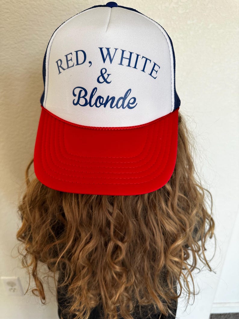 May include: A trucker hat with a white front panel, a red brim, and a navy blue mesh back. The hat features the text "RED, WHITE & Blonde" in navy blue script.