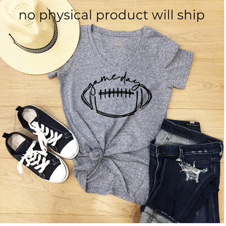 May include: A heather gray V-neck t-shirt with a black graphic of a football and the text "game day" in cursive script, paired with a straw hat, black canvas sneakers with white laces, and dark blue distressed denim jeans.