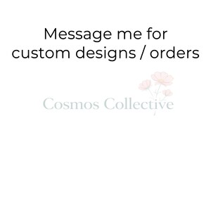 May include: A white graphic sign featuring the black text Message me for custom designs / orders at the top. Below this, the light gray text Cosmos Collective is displayed alongside a small illustration of three pale pink cosmos flowers.