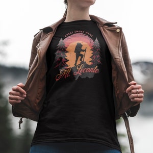 May include: A black t-shirt featuring a vintage-style graphic of a hiker in the Great Smoky Mountains. The graphic depicts a sunset, trees, and the text "Mt. LeConte".