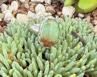 May include: A silver ring featuring a large, oval-shaped cabochon stone with a smooth, polished surface. The stone displays a gradient of light mint green at the top transitioning into a warm, earthy brown color at the base, set in a scalloped bezel.