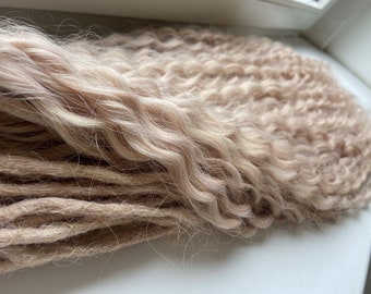 May include: A set of long, curly, light blonde and brown synthetic dreadlocks. The dreadlocks are arranged in a loose pile.