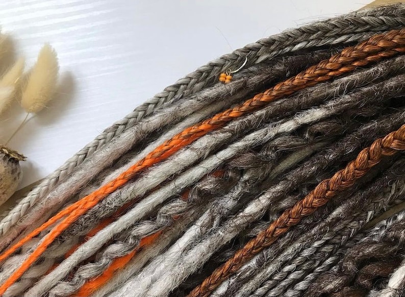 Peut inclure: Un ensemble de dreadlocks synth&eacute;tiques dans diff&eacute;rentes nuances de gris, de brun et d'orange. Les dreadlocks sont tress&eacute;es et ont une apparence textur&eacute;e.