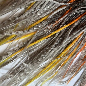 Peut inclure: Un paquet de dreadlocks synth&eacute;tiques de couleur gris, jaune et orange. Les dreadlocks sont faites de cheveux kanekalon et sont pr&ecirc;tes &agrave; &ecirc;tre install&eacute;es.
