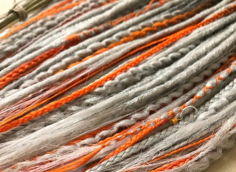 Peut inclure: Dreadlocks synth&eacute;tiques gris et orange. Les dreadlocks sont faites d'un mat&eacute;riau doux et textur&eacute; et ont un aspect naturel, l&eacute;g&egrave;rement d&eacute;sordonn&eacute;.