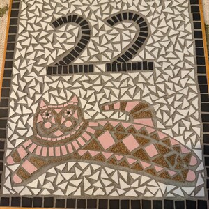 May include: Square mosaic tile featuring the number 22 in black and a pink cat design. The background is white and grey mosaic tiles. The border is black and the frame is wood.