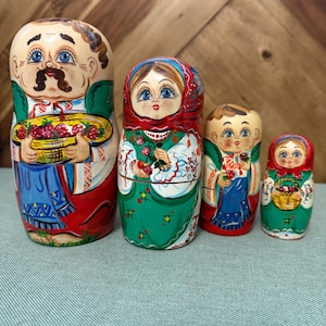 May include: A set of four Russian nesting dolls, each hand-painted with detailed facial features and traditional clothing. The dolls range in size, with the largest doll holding a basket of strawberries. The color palette includes red, green, blue, and beige.