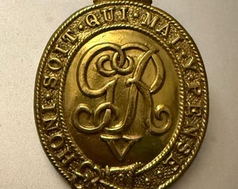 May include: A gold-colored metal badge with a crown on top and the words "South Australia Police" around the edge. The center of the badge features a stylized "R" with a crown above it.