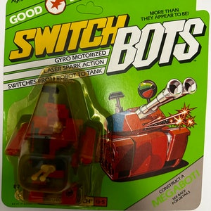 May include: A retro Switch Bots toy, packaged on a green and white card. The toy transforms from a red robot to a red tank. The packaging includes text such as "Gyro Motorized" and "Laser Spark Action". Suitable for ages 4 and up.
