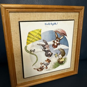 May include: Framed illustration of three brown rabbits flying kites in a blue sky with clouds. The text "Hold tight!" is written in blue at the top of the image.