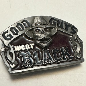 May include: A silver belt buckle with a skull wearing a hat and the words "Good Guys Wear Black" in black lettering.