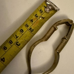 May include: A silver-toned nutcracker with a curved handle and a hinged jaw. The nutcracker is measured against a yellow tape measure.