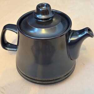 May include: A dark brown ceramic teapot with a lid. The teapot has a green band around the bottom.
