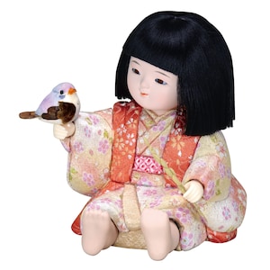 May include: A traditional Japanese doll wearing a pink and orange kimono with floral patterns. The doll has black hair and is holding a small blue bird in its hand.