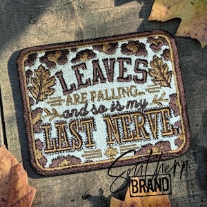 May include: A rectangular embroidered patch with a light blue background and a brown leopard print border. The text reads LEAVES ARE FALLING... and so is my LAST NERVE. The design includes embroidered oak leaf accents in shades of brown and gold.