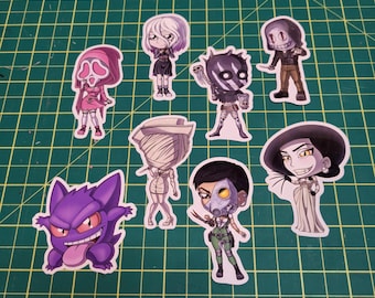 May include: A collection of die-cut stickers featuring various cartoon characters. The stickers include a purple Gengar, a pink Ghostface, and other stylized figures in a variety of outfits. The stickers are on a green cutting mat.