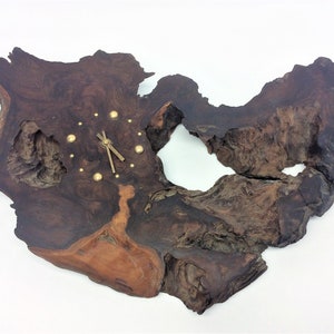 May include: A unique wall clock crafted from a dark brown, irregularly shaped piece of wood. The clock features gold-colored hands and hour markers, adding a touch of elegance to the rustic design.