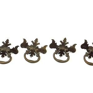 May include: Four antique bronze-colored drawer pulls. Each pull features a decorative leaf design and a circular handle. These vintage hardware pieces are ideal for furniture restoration projects.