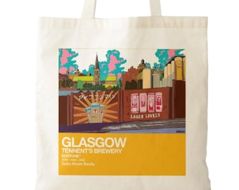 May include: A cream-colored canvas tote bag featuring a graphic illustration of the Tennent's Brewery in Glasgow. The print includes a cityscape, stylized beer cans, and text reading GLASGOW, TENNENT'S BREWERY, EDDTONE, 1885-1990-2023, Duke Street Swally.