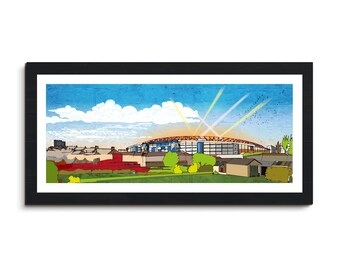 May include: A framed art print featuring a colorful illustration of a stadium under a blue sky with clouds and a setting sun. The artwork includes red, green, and brown buildings in the foreground, with a black frame.