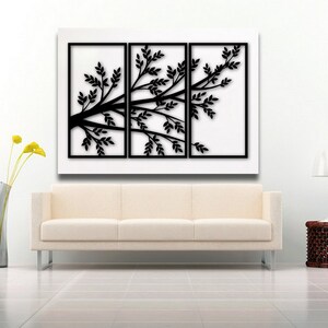May include: A black tree branch wall art piece with leaves, displayed in three framed panels. The artwork is set against a white background, above a cream-colored sofa. A modern home decor item.