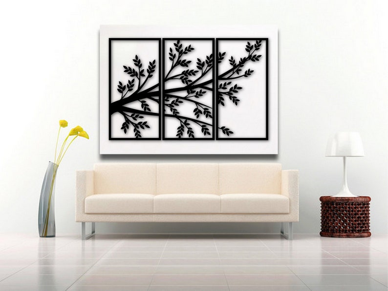 May include: A black tree branch wall art piece with leaves, displayed in three framed panels. The artwork is set against a white background, above a cream-colored sofa. A modern home decor item.