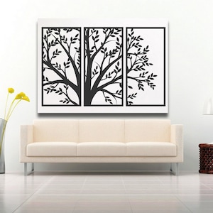 May include: A triptych wall art piece featuring a black tree silhouette with leaves against a white background. The artwork is displayed above a cream-colored sofa. A tall, slender vase with yellow flowers and a side table with a lamp are also in the room.